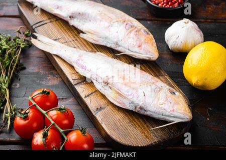 Roher frischer Meerbarben- oder Barabulka-Vollfisch mit Zutaten und Kräutern auf altem dunklem Holztisch Stockfoto