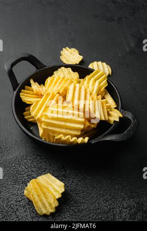 Wellige, leicht gesalzene Kartoffelchips auf schwarzem, dunklem Steintischhintergrund Stockfoto