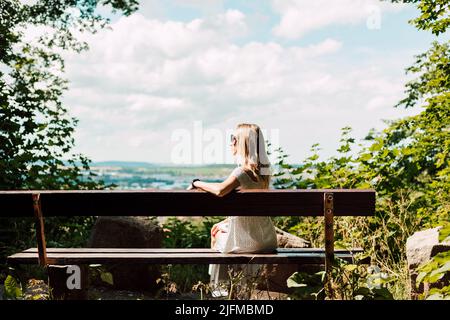 Eine Frau sitzt mit dem Rücken auf einer Bank und blickt auf die Stadt und die Berge Stockfoto