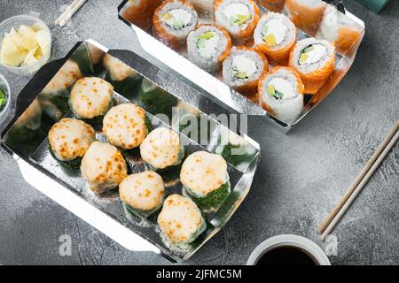 Leckere Sushi-Brötchen in Einwegboxen auf grauem Steinhintergrund Stockfoto