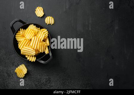 Gewellte Kartoffelchips mit Salz-Pfeffer-Geschmack auf schwarzem dunklen Steinhintergrund, flache Lage von oben, mit Platz für Text Stockfoto