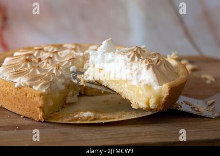 Zitronenmeringue in Scheiben geschnitten und mit einem Kuchenschneider serviert. Auf einem hölzernen Schneidebrett Stockfoto