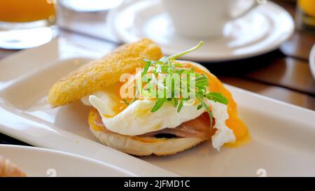 Egg Benedict auf dem Frühstückstisch im Restaurant. Essen im Hotel. Köstliches pochiertes Ei mit Schinken, Salat, Muffin-Brötchen und Sauce Hollandaise. Frühstück serviert Stockfoto