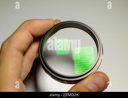 Ein Kind, das das Makroobjektiv in der Hand auf einem weißen Hintergrund hält. Lichtreflexion auf einer Glasoberfläche. Stockfoto