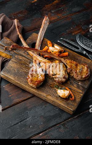 Hausgemachte gekochte Lammkoteletts mit Knoblauch und Karotten, auf hölzernem Servierbrett, auf altem dunklen Holztisch-Hintergrund, mit Kopierraum und Platz für Text Stockfoto