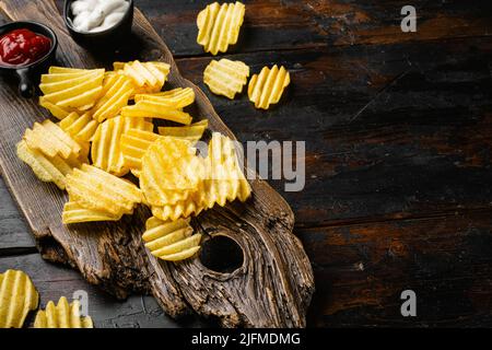 Wellige, leicht gesalzene Kartoffelchips auf altem dunklen Holztisch mit Platz für Text Stockfoto