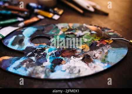 Palette in Farbe und ein Palettenmesser auf einem Holztisch. Stockfoto