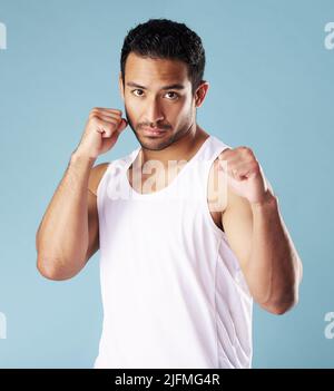 Hübscher junger hispanischer Mann in Boxerpose, der isoliert vor blauem Hintergrund im Studio steht. Gemischter Athlet mit einer Weste, bereit für eine Stockfoto