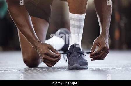 Nahaufnahme eines unbekannten afroamerikaners, der vor dem Training im Fitnessstudio kniet und Schnürsenkel bindet. Starker, ftiger, aktiver schwarzer Mann, der sich darauf vorbereitet Stockfoto