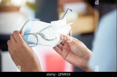 Eine unkenntliche Frau, die ihre Brille in ihrer Wohnung putzt. Eine unbekannte Frau, die ein Gewebe verwendet, um Staub von ihrer Brille zu entfernen Stockfoto