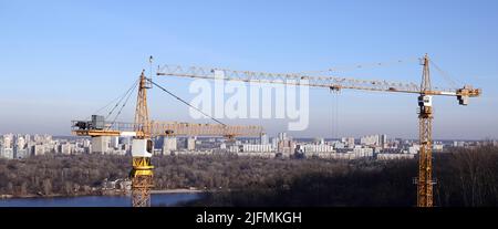 Hohe Baukräne auf dem Hintergrund der Häuser am linken Ufer der Stadt Kiew Stockfoto