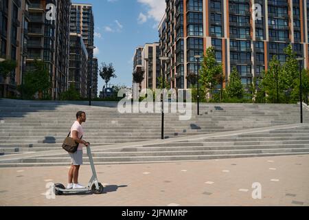 Junger Mann, der mit dem E-Scooter durch die Stadt kommt Stockfoto