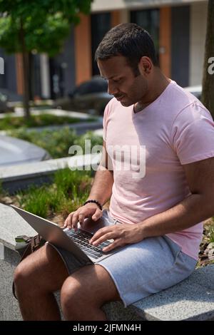 Konzentrierter Freiberufler, der mit seinem Laptop im Freien sitzt Stockfoto