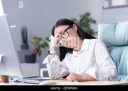 Eine traurige asiatische Geschäftsfrau verzweifelt an ihren Fähigkeiten, ist deprimiert und arbeitet im Büro am Computer. Stockfoto