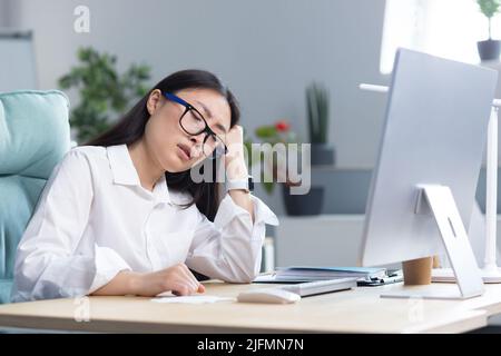 Eine traurige asiatische Geschäftsfrau verzweifelt an ihren Fähigkeiten, ist deprimiert und arbeitet im Büro am Computer. Stockfoto