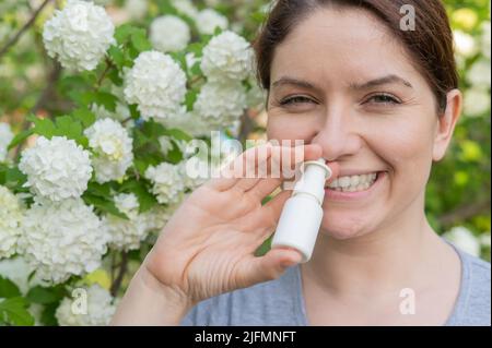 Kaukasische Frau verwendet ein Nasenspray, während sie im Park spazieren geht. Stockfoto