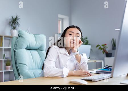 Eine traurige Geschäftsfrau arbeitet in einem modernen Büro, eine asiatische Frau denkt über die Ergebnisse der Arbeit nach. Stockfoto
