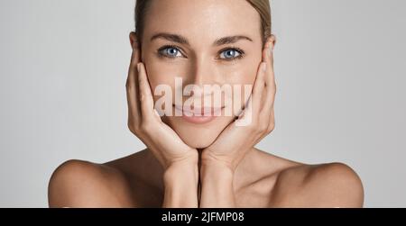 Hautpflege. Schöne Frau mit gesunder Gesichtshaut berühren Hände mit Feuchtigkeit befeuchten Gesichtshaut, auf hellgrauem Hintergrund. Hohe Qualität Stockfoto