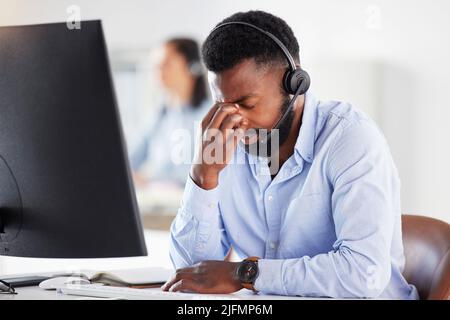 Einer betonte, dass der junge afroamerikanische männliche Callcenter-Agent Kopfschmerzen bekam, während er im Büro am Computer arbeitete. Berater macht Fehler und Stockfoto