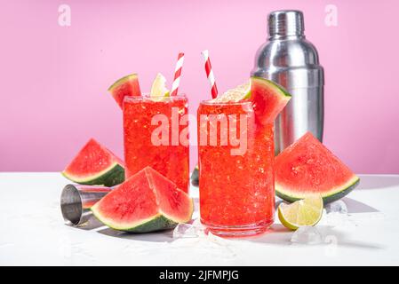 Cocktail aus Wassermelonen-Limonade mit Limette und in Scheiben geschnittener Wassermelone auf einem trendigen, hochfarbigen, weiß-rosa Hintergrund Stockfoto