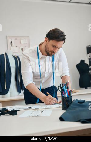 Couturier zeichnet Skizzen von Dingen in der Nähwerkstatt mit Bleistift Stockfoto