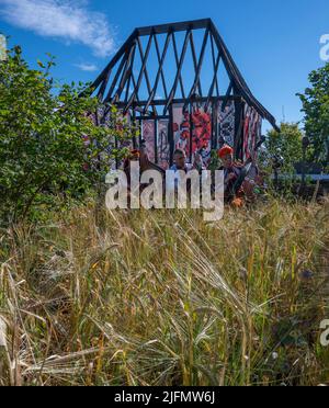 Hampton Court Palace, Surrey, Großbritannien. 4. Juli 2022. RHS Hampton Court Palace Garden Festival Pressetag für die größte Blumenschau der Welt, die bis zum 9. Juli 2022 stattfindet. Bild: Global Impact Garden: Traditionelle ukrainische Band tritt hinter Weizenfeldern auf dem von Victoria Manoylo und Carrie Preston entworfenen „What does Not Burn Garden“ auf, einer Destillation der ukrainischen Landschaft und Kultur. Es zeigt den Rushnyk, ein besticktes Tuch, das in vielen Ritualen verwendet wird, als Symbol des Lebens und der Identität. Wie eine neue Haut schmücken Rushnyks die Überreste einer verbrannten Hütte, die als Silhouette in der Landschaft steht. Kredit: Ma Stockfoto