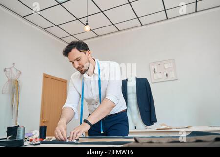 Couturier in der Nähwerkstatt kreiden Muster auf einem schwarzen Stoff Stockfoto