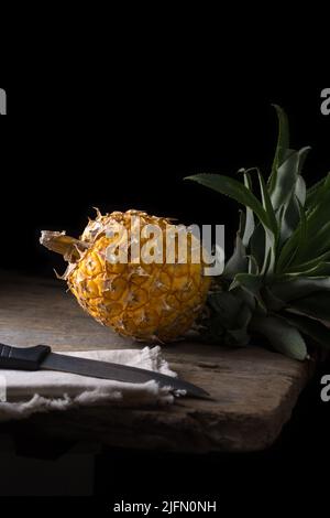 Ananas, tropische Früchte auf einer Tischplatte, mit einem Messer vorne, dunkler Hintergrund mit Kopierfläche Stockfoto