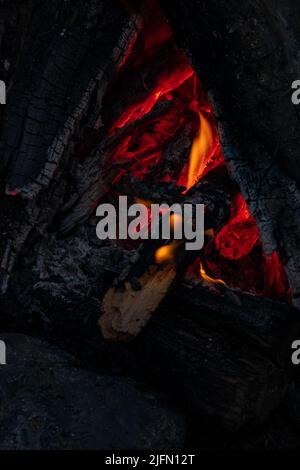 Helle Flamme eines brennenden Feuers auf dunklem Hintergrund. Zeitlupe. Funken und Flammen. Brennendes Lagerfeuer. Brennholz brennt im Feuer. Stockfoto