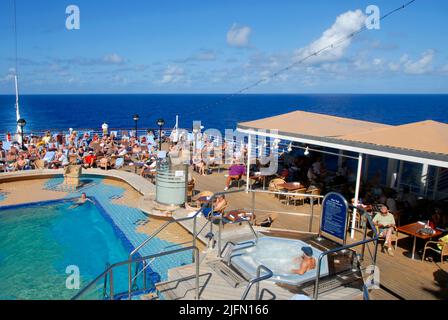 Passagiere entspannen sich am Pool im Heck eines Kreuzfahrtschiffes auf See in der Karibik Stockfoto