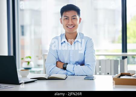 Asiatischer Geschäftsmann, der an seinem Laptop arbeitet. Porträt eines jungen asiatischen Geschäftsmannes, der in einem modernen Büro arbeitet. Glücklicher Geschäftsmann, der auf seinem Laptop tippt Stockfoto