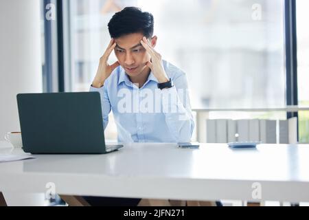 Ein junger asiatischer Geschäftsmann, der erschöpft, müde und unmotiviert aussah, während er auf einen langsamen Laptop-Verbindungsfehler wartete. Fauler Mann, der nachlappte und ignorierte Stockfoto