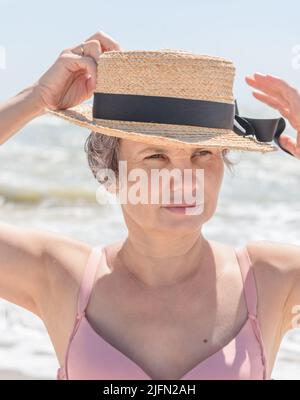 Porträt einer verheirateten grauhaarigen Frau in Bootsanzug und Badeanzug, die auf verschwommenem Meereshintergrund mit Wellen in die Ferne blickt.Konzept der natürlichen Schönheit. Stockfoto