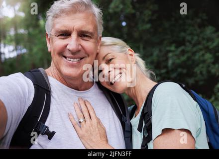 Porträt eines älteren kaukasischen Paares, das lächelt und während einer Wanderung im Freien ein Selfie in einem Wald aufnimmt. Mann und Frau zeigen Zuneigung und Stockfoto