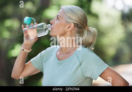Nach ihrem morgendlichen Lauf kühlte sie sich ab. Aufnahme einer reifen Frau, die während des Trainings im Freien Wasser trinkt. Stockfoto