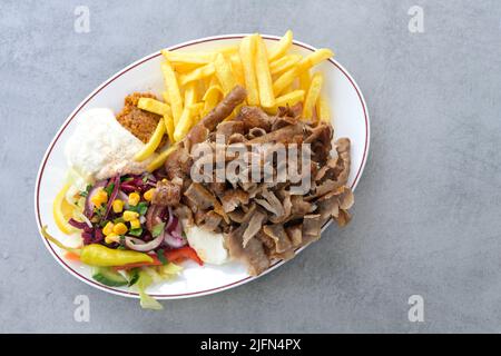 Döner Kebab, Fleischscheiben aus einem rotierenden Spieß mit Salat, pommes frites und Joghurt-Dip-Sauce auf einem ovalen Teller und einem grauen Tisch, Kopierraum, hoher Angl Stockfoto