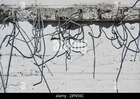 Verstärkungsstäbe nach dem Abriss stecken nutzlos aus einer hellen Betonwand und werfen Schatten, abstrakter Grunge-Hintergrund für Architektur und Gebäude Stockfoto