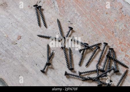 Schwarze Metallschrauben liegen auf dem Betonboden, Schrauben auf Holz. Stockfoto