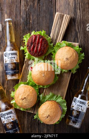 30.06.2022; Berlin; Deutschland; Korona-Bier und frische leckere Burger mit saftigen Fleischpasteten; Ketchup und Kräuter auf einem hölzernen Vintage-Tisch; Draufsicht; Resta Stockfoto