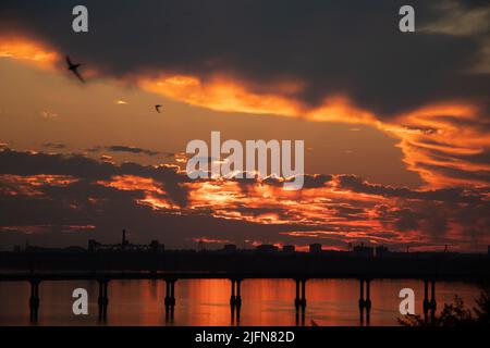 Sonnenuntergang auf dem Dnepr Fluss über der Brücke in der Ukraine in der Stadt Dnepr während des Krieges, Abenduntergang in der Stadt Stockfoto