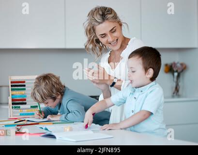 Alleinerziehende Mutter, die kleine Söhne während des Homeschool-Unterrichts zu Hause unterrichtet. Autistische niedliche kleine kaukasische Jungen lernen während ihrer Zeit lesen und schreiben Stockfoto