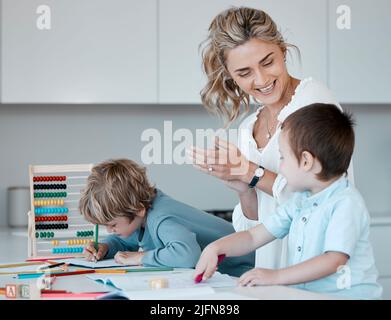 Alleinerziehende Mutter, die kleine Söhne während des Homeschool-Unterrichts zu Hause unterrichtet. Autistische niedliche kleine kaukasische Jungen lernen während ihrer Zeit lesen und schreiben Stockfoto