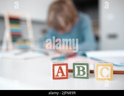 Nahaufnahme von hölzernen Spielzeugblöcken auf einem Tisch zu Hause. Ein kleiner Junge verschwimmte im Hintergrund, spielte, machte seine Hausaufgaben und machte eine Ausbildung durch Stockfoto