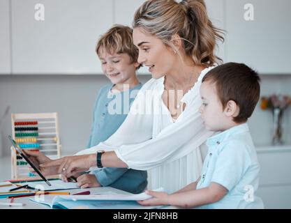 Alleinerziehende Mutter, die kleine Söhne während des Homeschool-Unterrichts zu Hause unterrichtet. Autistische niedliche kleine kaukasische Jungen lernen während ihrer Zeit lesen und schreiben Stockfoto