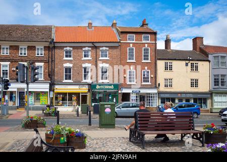 Die High Street der Marktstadt Stokesley North Yorkshire an einem sonnigen Sommertag mit einem Paar auf einer Bank in der Nähe der Kreuzung Stockfoto