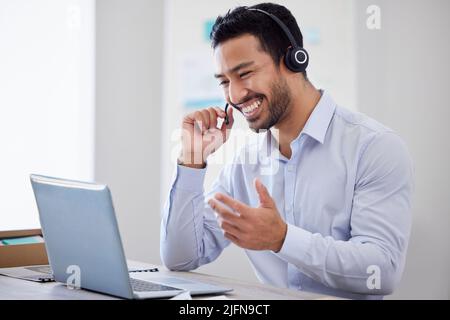 Ein glücklicher Mann, der in einem Callcenter arbeitet. Bediener, der einen Laptop und ein Headset verwendet, online beraten oder einen Videoanruf tätigen kann. Ein männlicher Kundendienstmitarbeiter oder Stockfoto