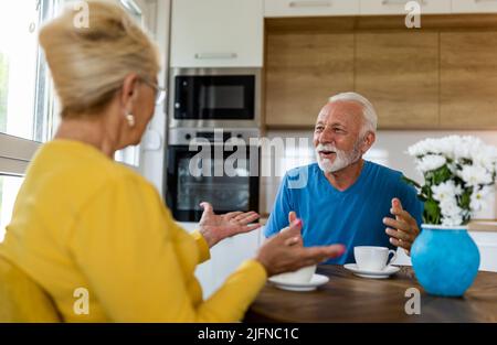 Seniorenpaar sitzt am Esstisch in der Küche, trinkt Kaffee und redet Stockfoto