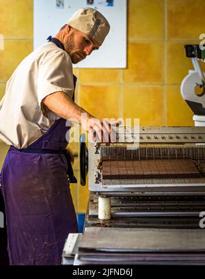 Mitarbeiter der Chocolaterie Frigoulette in Beaufort-sur-Gervanne (die, Frankreich) schneiden Nougatpralinen. Die geschnittene Praline kommt ohne zusätzliche Schokoladenschale. Die Manufaktur verwendet ausschließlich zertifizierte Bio- und Fair-Trade-Kakaobohnen von São Tomé. Stockfoto