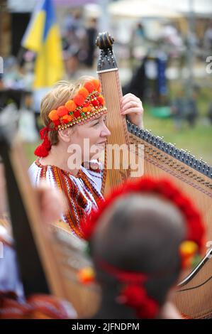 Hampton Court Palace, Surrey, Großbritannien - 04.06.2022, ukrainische Musiker spielen traditionelle Musik im What does Not Burn Garden. Das verwendete Instrument ist eine Bandura oder Kobza (auch bekannt als die "ukrainische Harfe"). Der Garten, der im RHS Hampton Court Palace mit dem Best Global Impact Garden Award ausgezeichnet wurde, ist eine Destillation der ukrainischen Landschaft und Kultur. Es zeigt den Rushnyk, ein besticktes Tuch, das in vielen Ritualen verwendet wird, als Symbol des Lebens und der Identität. Die seit 1993 stattfindende Messe ist die prestigeträchtigste Blumen- und Gartenveranstaltung im Vereinigten Königreich und die größte jährliche Blume der Welt Stockfoto