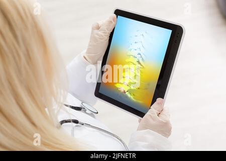 Arzt beobachtet eine Röntgenaufnahme von Hüfte und Wirbelsäule auf Rückenschmerzen auf einem digitalen Tablet. Stockfoto